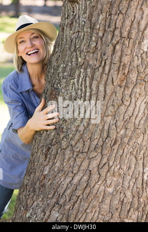 Frau versteckt sich hinter Baumstamm Stockfoto