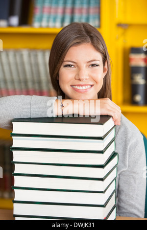 Glückliche Frau ruht Kinn auf gestapelten Bücher In der Bibliothek Stockfoto