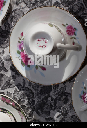 Teetasse kopfüber auf eine Untertasse auf einem gemusterten Tischdecke. Stockfoto