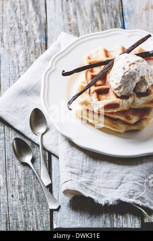 Weißer Teller mit frischen Waffeln, serviert mit Eis und Vanille Stangen über Holztisch. Stockfoto