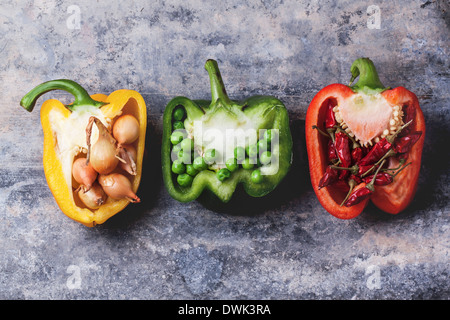 Die Hälfte der Rohe rote, grüne und gelbe Paprika gefüllte kleine Zwiebeln, Erbsen und red hot Chili Paprika über Vintage-Hintergrund. Stockfoto