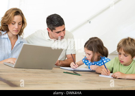 Mutter mit Laptop während Vater unterstützt Kinder in der Färbung Stockfoto