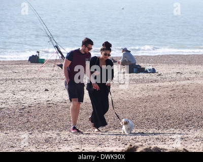 Ein paar, die ihren Hund spazieren gehen, am Strand von Eastney in Portsmouth, Hampshire Stockfoto