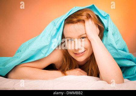 Frau liegend auf Kissen im Bett, bedeckt mit blauen Decke Stockfoto