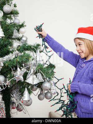 Mädchen schmücken Weihnachtsbaum mit Lichterketten Stockfoto