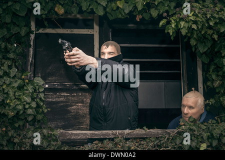 Zwei maskierte bewaffnete Männer verstecken auf bewachsenen Veranda der alten Kabine. Stockfoto