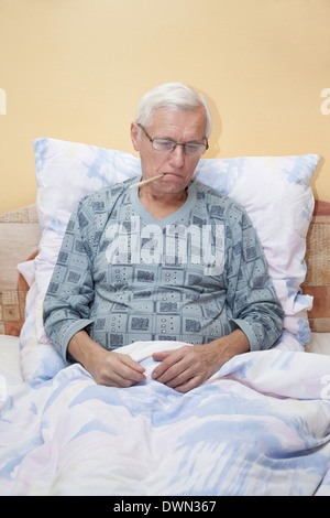 Kranker senior Mann prüfen Temperatur mit Thermometer im Bett. Stockfoto