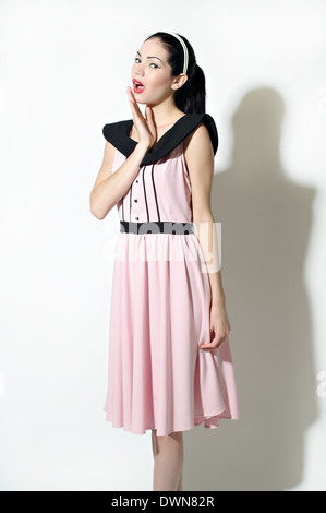 Eine schöne Retro-Frau im Pferdeschwanz ist überrascht, stehend und gekleidet in einem Vintage inspirierte 50er Jahre Kleid, ein Vintage-Konzept Stockfoto