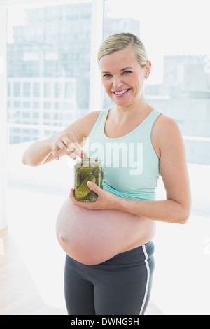 Lächelnde blonde schwangere Frau aus Glas Gewürzgurken Essen Stockfoto