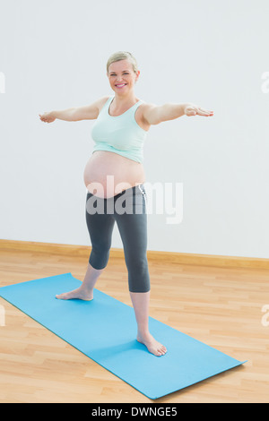 Blonde schwangere Frau tun Yoga am blauen Matte lächelnd in die Kamera Stockfoto