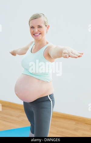 Blonde schwangere Frau beim Yoga auf der Matte lächelnd in die Kamera Stockfoto