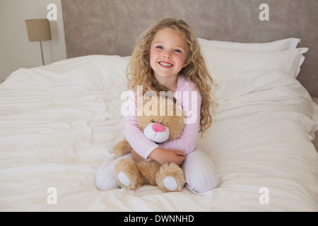 Glückliche Mädchen mit Stofftier sitzt auf Bett Stockfoto