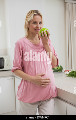 Schwangere Frau hält Apfel in Küche Stockfoto