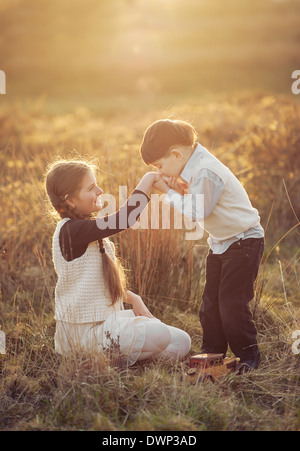 niedliche kleine Junge hand intelligent Dressefkisses Mädchen auf Sonnenuntergang im Feld Stockfoto