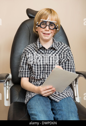 Junge mit Trial Frame hält Testchart bei Optiker Stockfoto
