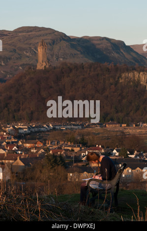 Ein Mädchen auf einer Bank auf Gowan Hügel in der Nähe von Stirling Castle zu studieren. Das Wallace-Monument ist in Ferne zu sehen. Stockfoto