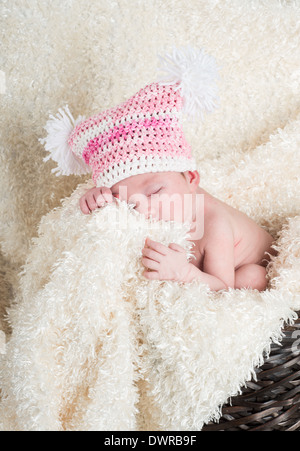 Schöne Neugeborenen einen rosa Hut mit weißen Pompons in einem braunen geflochtenen Korb auf einer weichen Creme farbige Decke schlafen Stockfoto