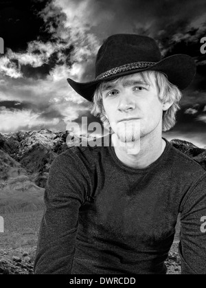 Monochrom hübscher junger Cowboy mit Bergen und einem dramatischen Himmel im Hintergrund Stockfoto