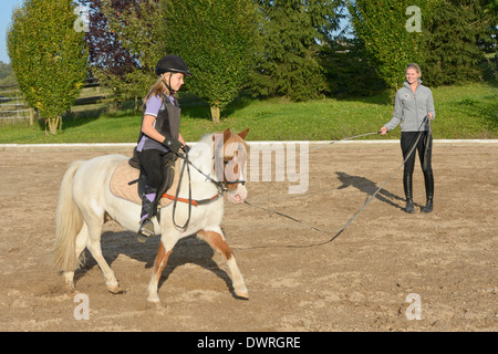 Mädchen tragen einen Körperschutz mit einem Ausfallschritt Lektion auf ein Pony im Trab Stockfoto