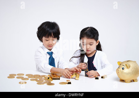 Kinder tragen Business-Kleidung an einem Tisch mit Münzen und Goldbarren Stockfoto