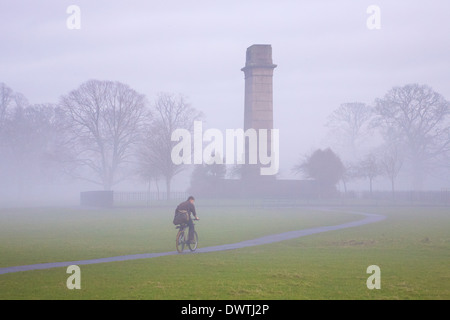 Mann, Radfahren auf einem Weg der Kenotaph Weltkrieg ein Denkmal im Nebel. Rickerby Park Carlisle, Cumbria, England. Stockfoto