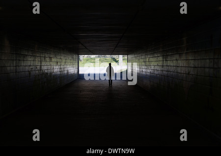 Silhouette einer Person zu Fuß durch eine dunkle Unterführung symbolisiert Licht am Ende des Tunnels Stockfoto