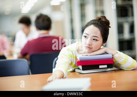 ein Mädchen, stützte sich auf einen Stapel Bücher in der Bibliothek Stockfoto