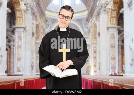 Junge männliche Priester zeigt auf einen Absatz mit der Bibel in einer Kathedrale Stockfoto