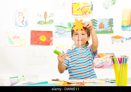 Junge in der frühen Entwicklungsklasse geschnitten, Papier und Klebstoff hält Papier Maple Leaf und Kleber Stock Stockfoto