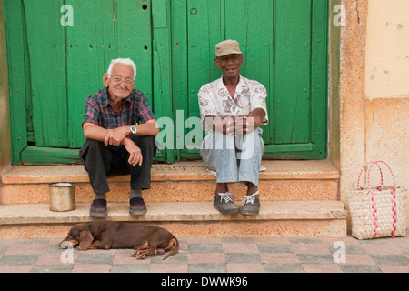 Zwei alte kubanische Männer mit einem Hund sitzt vor Haustür, Trinidad, Kuba Stockfoto