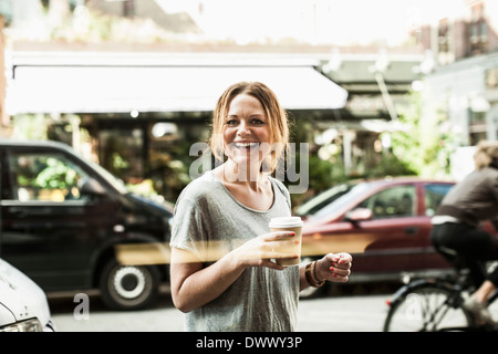 Porträt von glücklich Frau mit Einweg-Kaffeetasse auf Straße Stockfoto