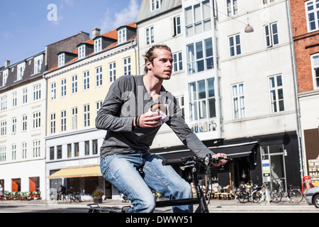 Junger Mann Betrieb Burger beim Reiten Fahrrad auf Stadtstraße Stockfoto