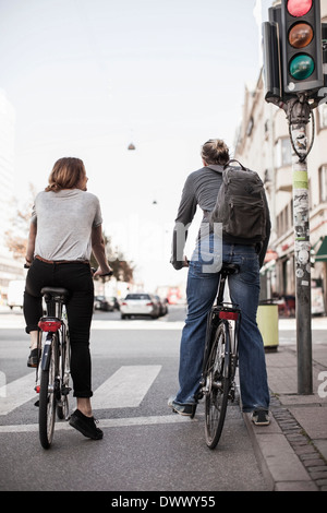 Rückansicht des Paares mit Fahrrädern warten auf Signale an Stadtstraße Stockfoto