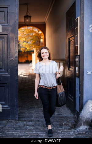 In voller Länge Portrait von glückliche Frau, die die Geldbörse zu Fuß gegen die Tür Stockfoto