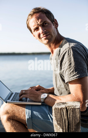 Reifer Mann wegsehen während mit Laptop am pier Stockfoto