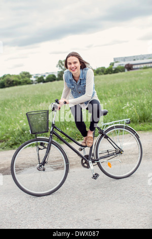 Porträt der glückliche junge Frau sitzt mit dem Fahrrad auf Land Stockfoto