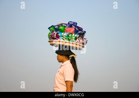 Eine Frau, die als Lebensmittel Anbieter arbeitet gleicht einem Tablett auf dem Kopf am Ufer des Mekong-Flusses in Phnom Penh, Kambodscha. Stockfoto
