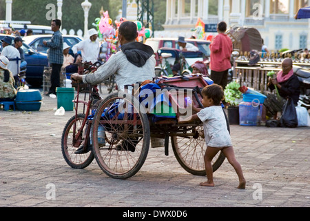 Ein Junge treibt einen behinderten Mann, die auf einen Rollstuhl angewiesen auf der Mekong-Uferpromenade in Phnom Penh, Kambodscha. Stockfoto