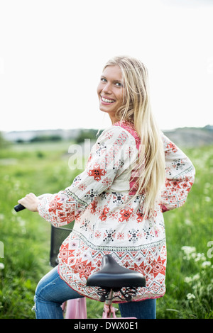 Hintere Ansicht Porträt der jungen Frau mit Fahrrad auf Feld Stockfoto