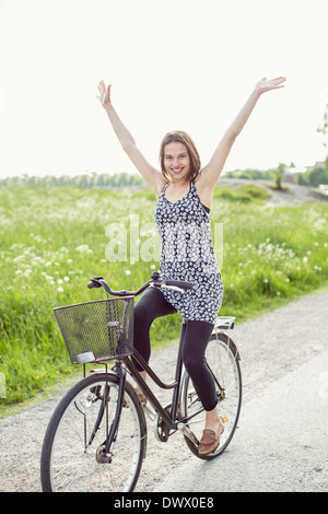 Porträt der glückliche Frau mit erhobenen Armen Radfahren auf Landstraße Stockfoto