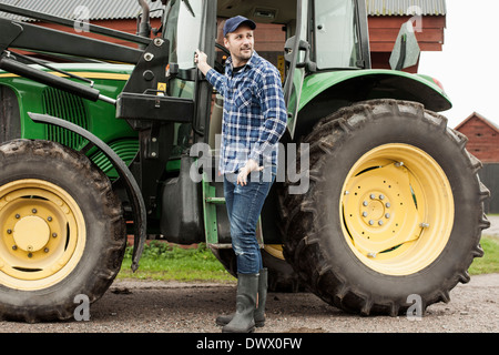 Voller Länge Bauern stehen mit einem Traktor auf Bauernhof Stockfoto