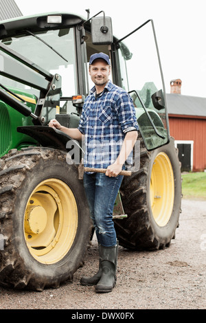 In voller Länge Portrait von Bauer mit Hammer tatenlos Traktor auf Bauernhof Stockfoto