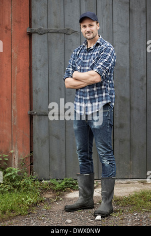 In voller Länge Portrait von zuversichtlich Bauer stehend Arme gekreuzt gegen Scheune Stockfoto