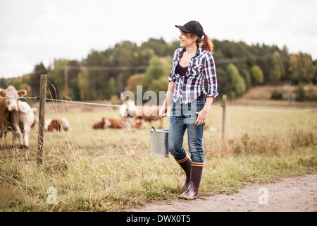 Bäuerin mit Eimer zu Fuß, während Tiere grasen im Feld Stockfoto