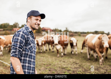 Lächelnde Landwirt wegsehen bei Field während Tiere grasen im Hintergrund Stockfoto