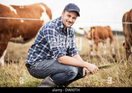 Porträt von Bauer mit Rasen hocken auf Feld während Tiere grasen im Hintergrund Stockfoto