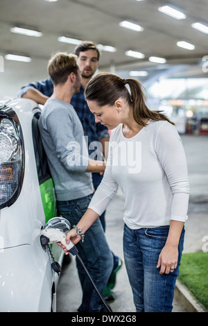 Frau Elektroauto mit Freunden stehen im Hintergrund an Tankstelle aufladen Stockfoto