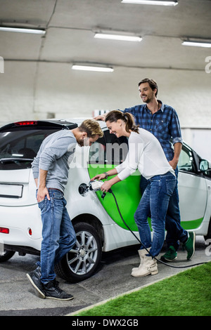 Männliche Freunde mit Frau Elektroauto an Tankstelle aufladen Stockfoto