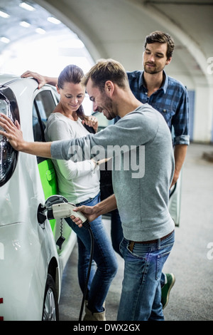 Freunde Blick auf Menschen, die Elektro-Auto in Tankstelle aufladen Stockfoto