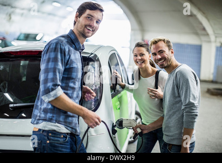 Porträt der happy Friends mit Mann Aufladen von Elektroautos an Tankstelle Stockfoto